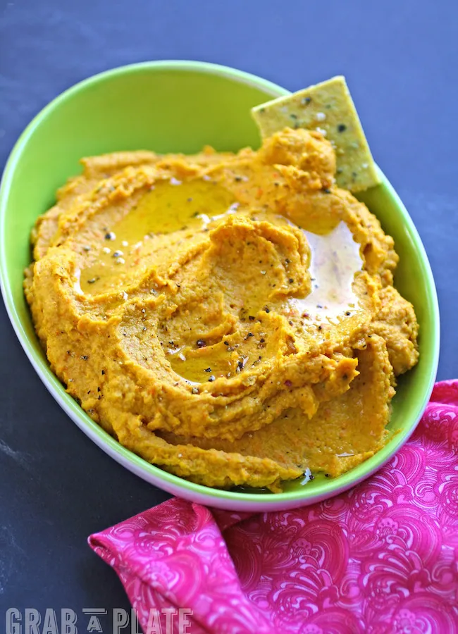 A bowl of colorful Carrot Hummus served with Curried Hemp Seed Crackers