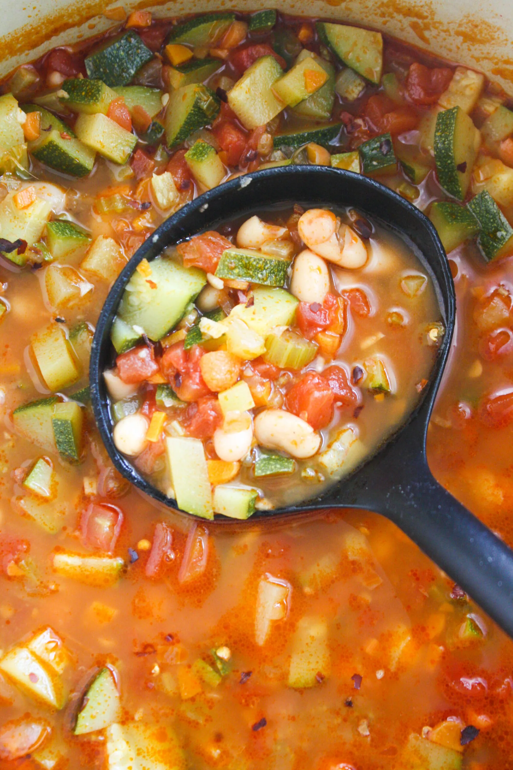 A ladle in a pot of White Bean and Zucchini Soup